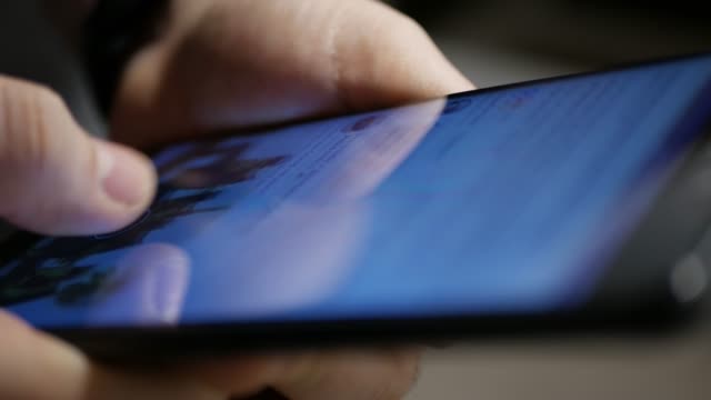 An extreme closeup with shallow DOF shot of someone scrolling through social media posts on a smartphone's touchscreen.