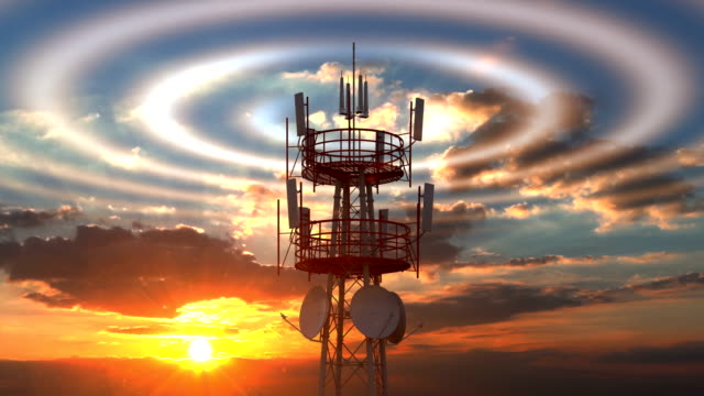 Cellular telecommunications tower with radio waves visible against sunset sky