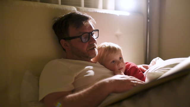 Father reading bedtime stories to child. Dad putting son to sleep.