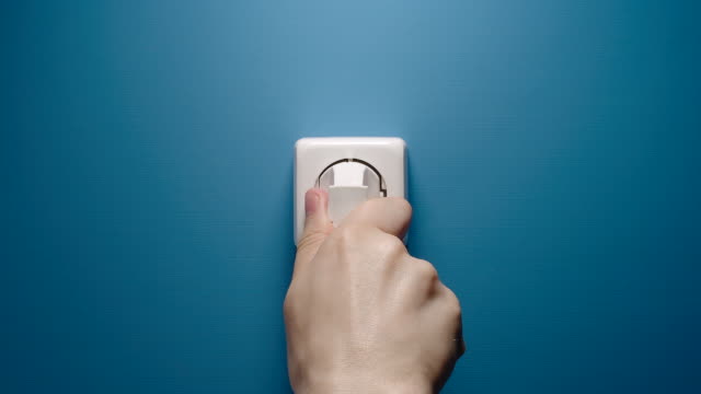 Man Inserts Plug Into Electrical Socket On A Blue Wall