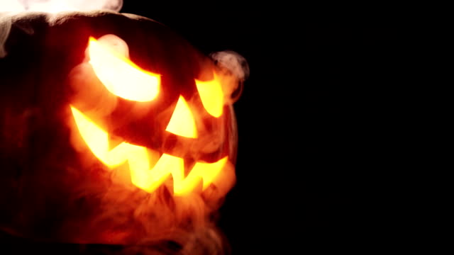 Shining Jack-O-Lantern. Halloween pumpkin with scary face smoke inside with flame isolated on the black background