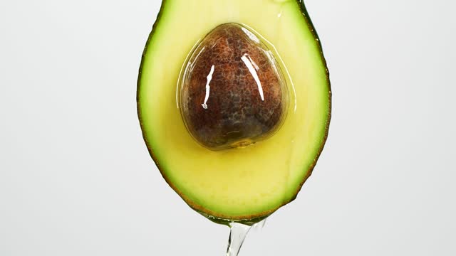 Slow motion close-up of fresh avocado fruit and oil flowing on white background