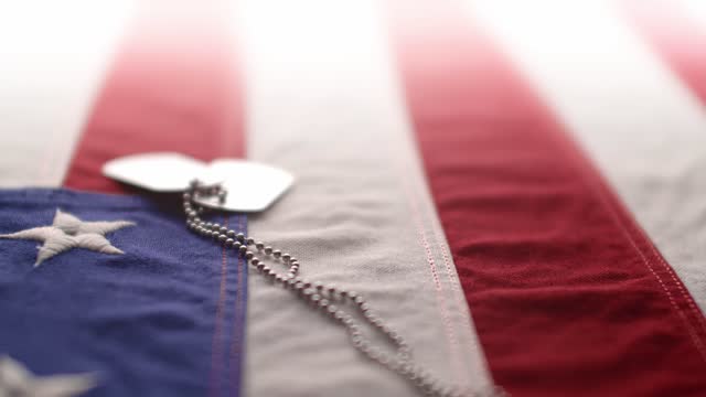 Slow motion of a US American flag with shiny military dog tags. Background for Armed Forces Day, Memorial Day, Veteran's Day, 4th of July, or other patriotic USA holiday.