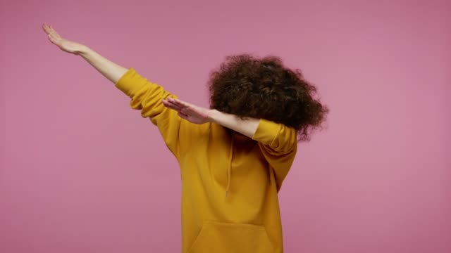 Trendy girl afro hairstyle in hoodie performing dab dance with serious calm face and making dabbing movement