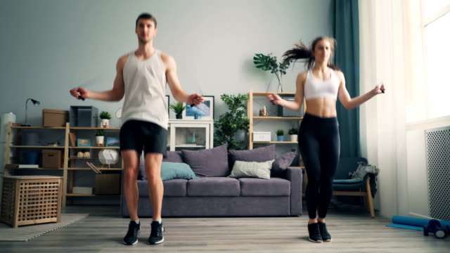 Young man and woman couple jumping rope in house together doing sports indoors