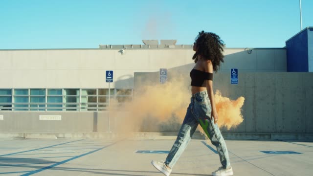 Young woman dancing outside with smoke grenade at sunset on rooftop parking garage
